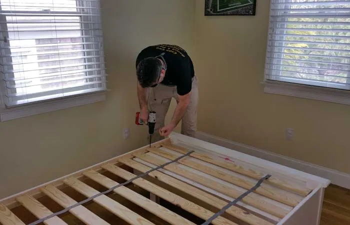 Mover reassembling a bed frame with a drill in a bedroom